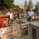 Friends enjoying alfresco dinner around outdoor kitchen