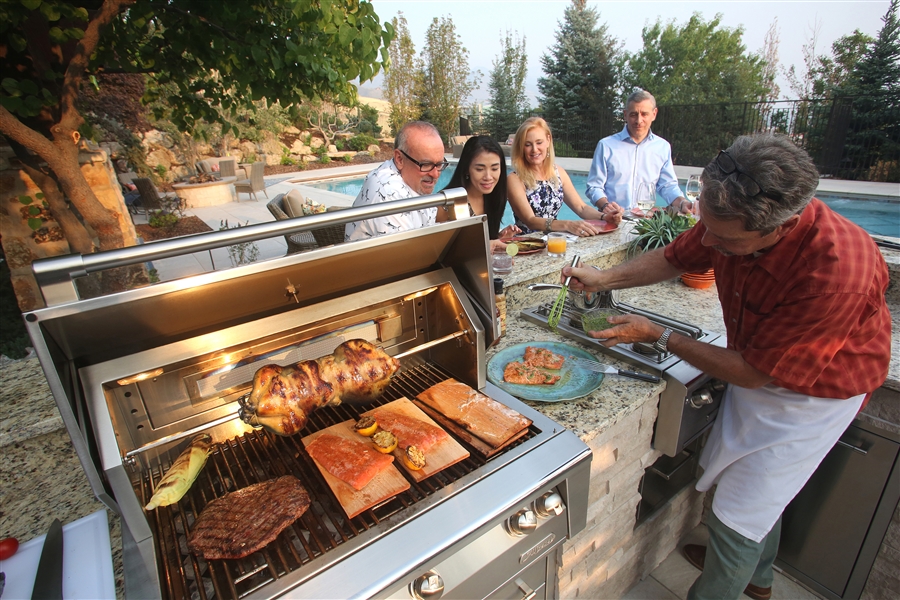 man cooking for group on outdoor grill as part of outdoor kitchen area